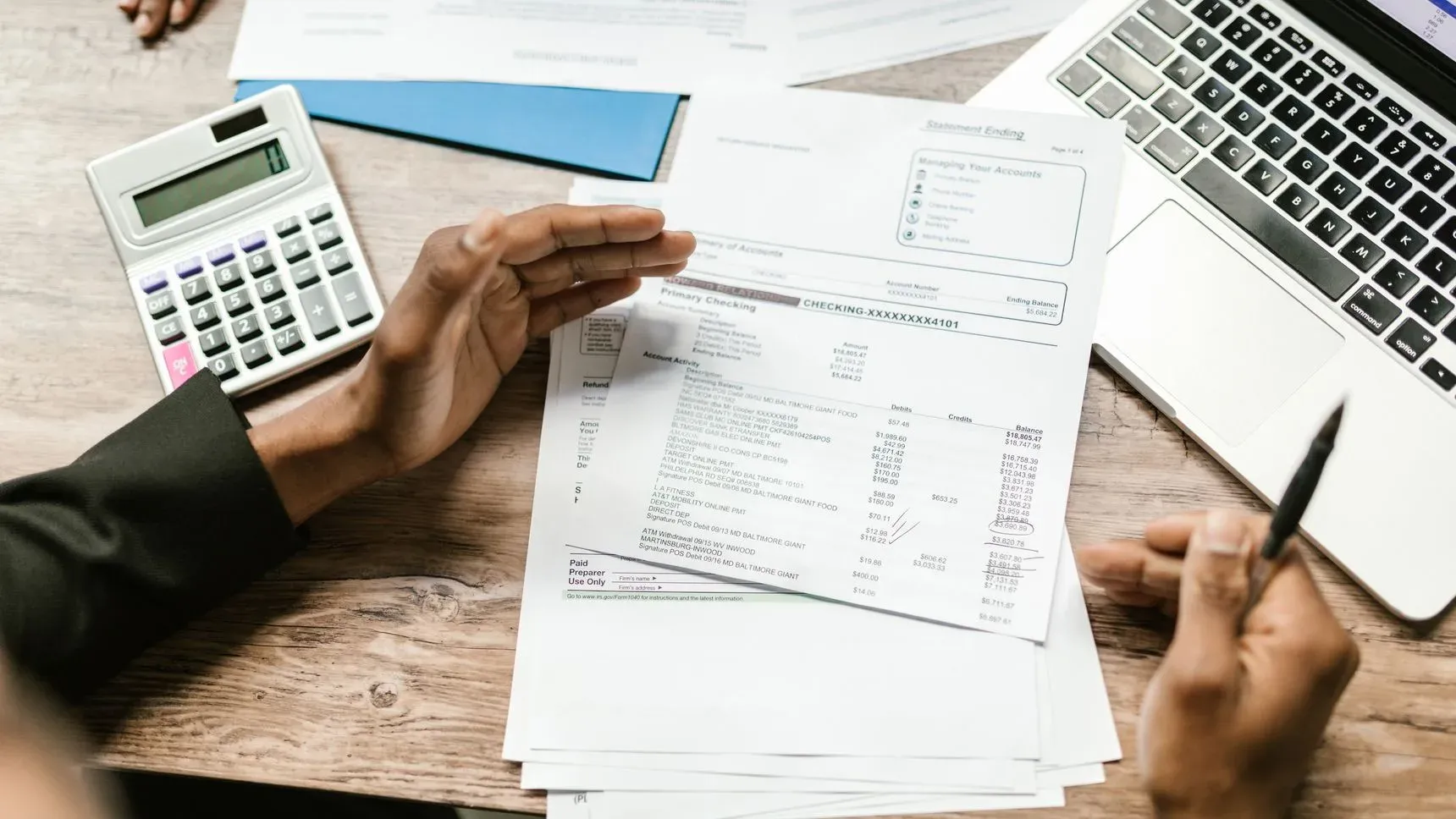 Hands holding documents next to a calculator and laptop on a desk
