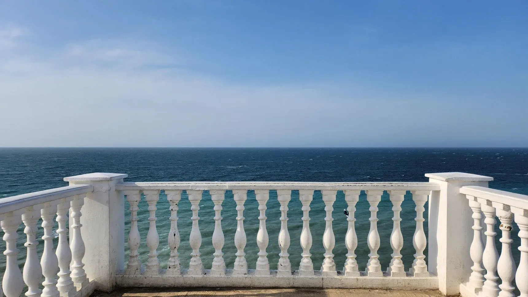 An empty balcony overlooking the sea under a clear sky