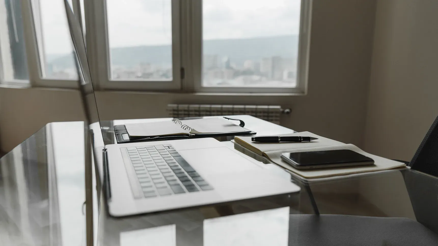 A desk by a window with a laptop and sorted paperwork in calm daylight